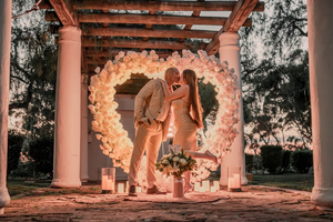 Romantic proposal leading to wedding: Couple kissing in front of illuminated floral heart with candles at outdoor venue.
