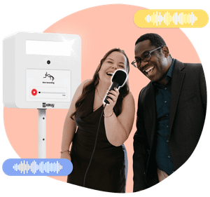 Two happy people holding a microphone in front of a KRUU photo booth, using the audio feature.