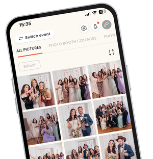 A close-up, angled view of a smartphone displaying the KRUU mobile app interface. The screen shows a digital photo gallery titled "Alle Bilder" (All Images) filled with various group photos taken at a wedding. The photos feature guests in formal attire posing with fun props like heart-shaped glasses and "Just Married" signs. The app design is clean and modern, featuring navigation icons for settings, notifications, and sharing at the top.
