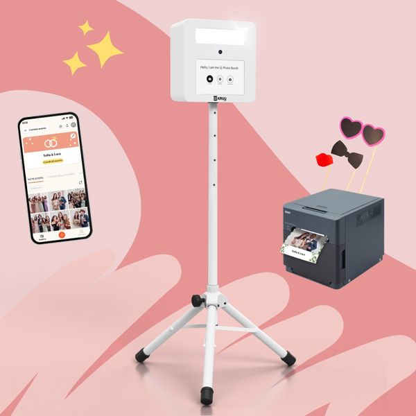 Un layout di prodotto su sfondo rosa con al centro una cabina fotografica KRUU bianca su un cavalletto. A sinistra, uno smartphone mostra una galleria digitale dell'evento all'interno dell'app KRUU. A destra, una stampante DNP grigio scuro mostra una foto appena stampata di una coppia. Sopra la stampante sono montati tre oggetti di scena come occhiali a forma di cuore, papillon e bocca da bacio.