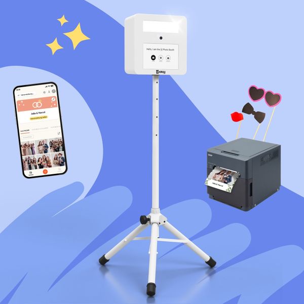 Ein Produktlayout auf blauem Hintergrund mit einem weißen KRUU-Fotostand auf einem Stativ in der Mitte. Auf der linken Seite ist ein Smartphone zu sehen, das eine digitale Event-Galerie in der KRUU-App anzeigt. Auf der rechten Seite steht ein dunkelgrauer DNP-Drucker mit einem frisch gedruckten Foto eines Paares. Über dem Drucker sind drei Fotorequisiten wie eine herzförmige Brille, eine Fliege und ein Kussmund aufgebaut.