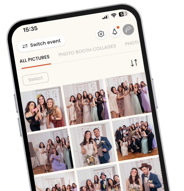 A close-up, angled view of a smartphone displaying the KRUU mobile app interface. The screen shows a digital photo gallery titled "Alle Bilder" (All Images) filled with various group photos taken at a wedding. The photos feature guests in formal attire posing with fun props like heart-shaped glasses and "Just Married" signs. The app design is clean and modern, featuring navigation icons for settings, notifications, and sharing at the top.